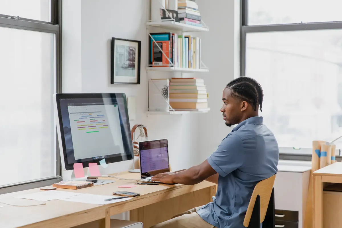 Focused man at home office desk working on dual screens. Ideal for remote work themes.